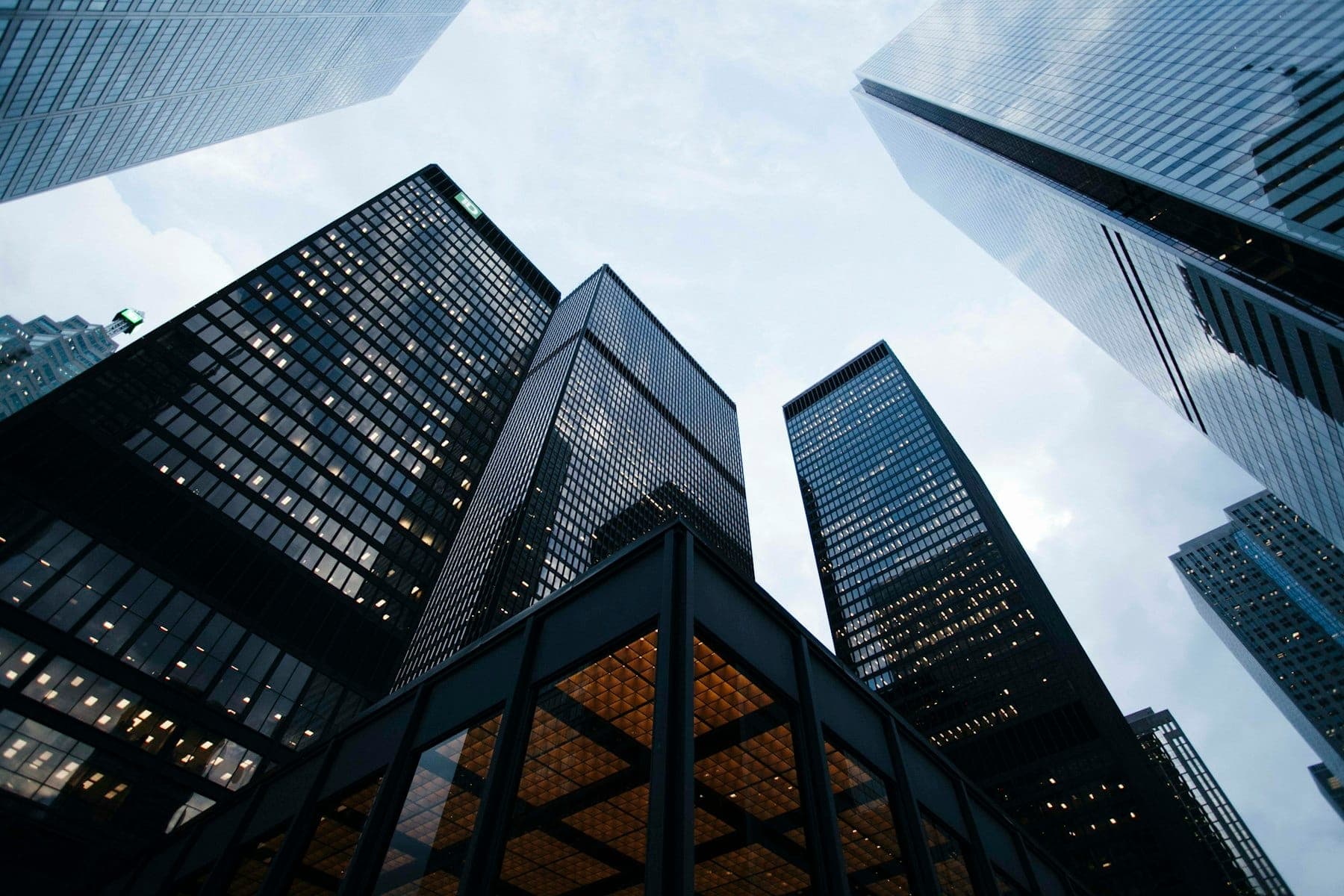 Looking up at dark glass high-rise towers against a pale sky